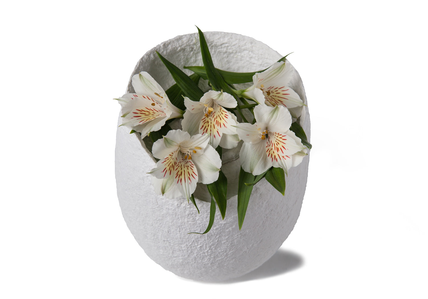 Picture of an ovoid biodegradable cremation urn made of white cotton fibre on sale at Muses Design Urns. View with flowers.