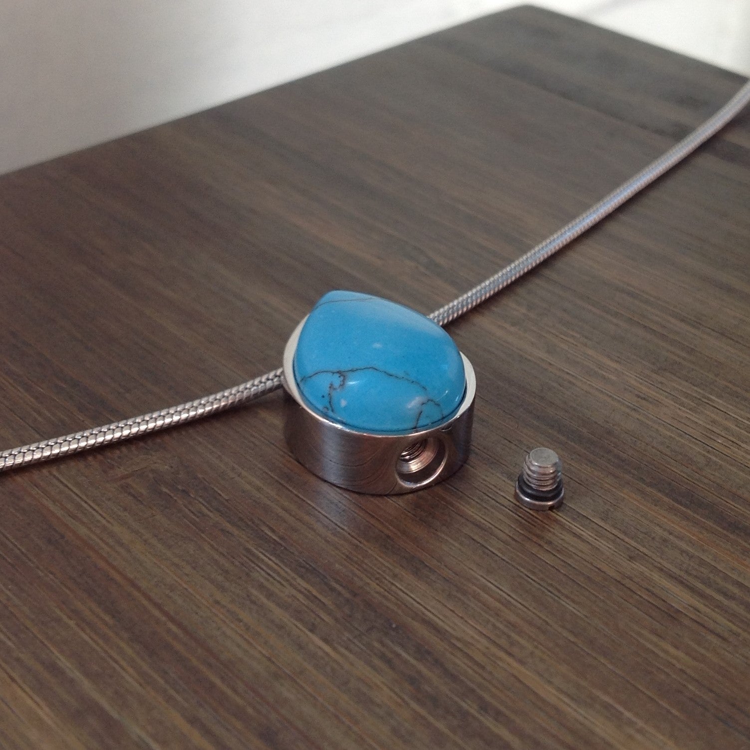Picture of a Stainless Steel  cremation jewelry with a small-drop pendant for ashes - top opening